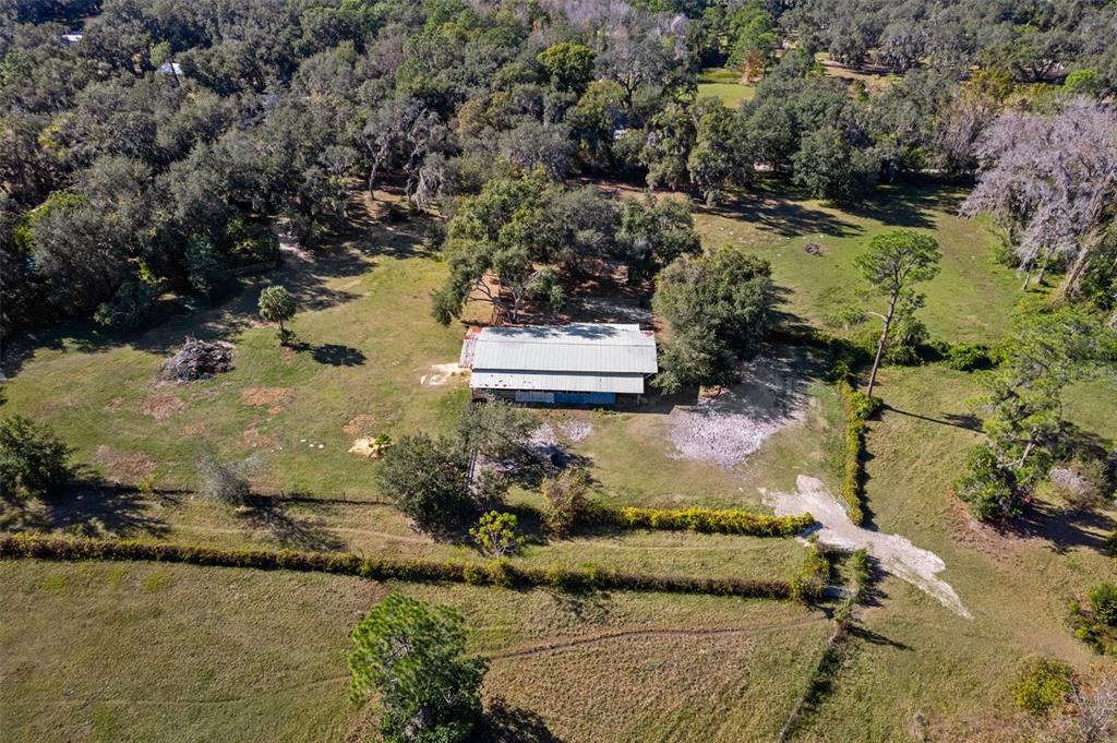 An aerial view shows a metal-roofed barn situated in a large, tree-lined grassy field — 27910 DEBBIE ROAD, OKAHUMPKA, FL