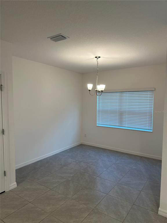 A dining area features gray tile flooring, a chandelier, and a window with white blinds — 189 GLASS ONION DRIVE, GROVELAND, FL