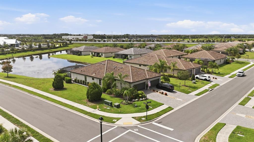 An aerial view shows a suburban neighborhood with houses, a pond, and paved streets — 16120 SUNNY DAY DRIVE, BRADENTON, FL