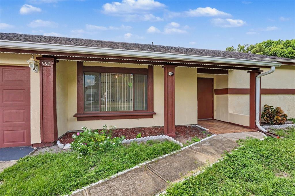 A single-story house exterior features a brown front door, a large window, and a walkway — 997 MARIPOSA DRIVE NE, PALM BAY, FL