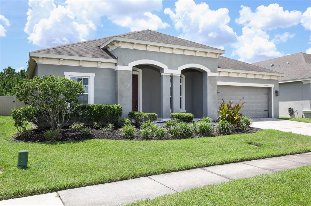 A gray single-story house features a covered entryway, a two-car garage, and a landscaped yard — 12397 STONE BARK TRAIL, ORLANDO, FL