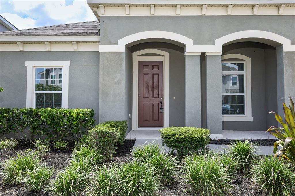 A gray house exterior features a brown front door, arched entryways, and manicured landscaping — 12397 STONE BARK TRAIL, ORLANDO, FL