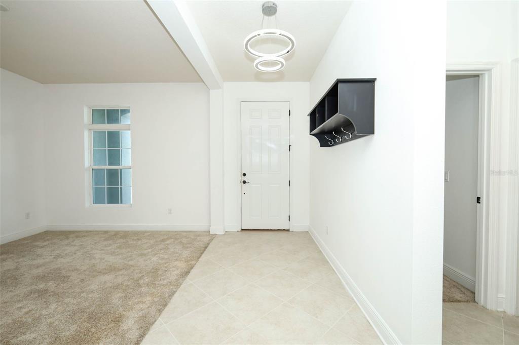 An entryway with tiled flooring, a coat rack, and an adjacent carpeted living area — 12397 STONE BARK TRAIL, ORLANDO, FL