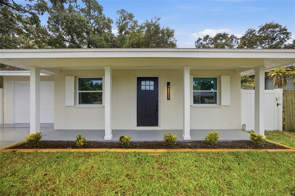 A single-story house exterior features a covered front porch, a dark door, and landscaping — 1333 OVERLEA STREET, CLEARWATER, FL