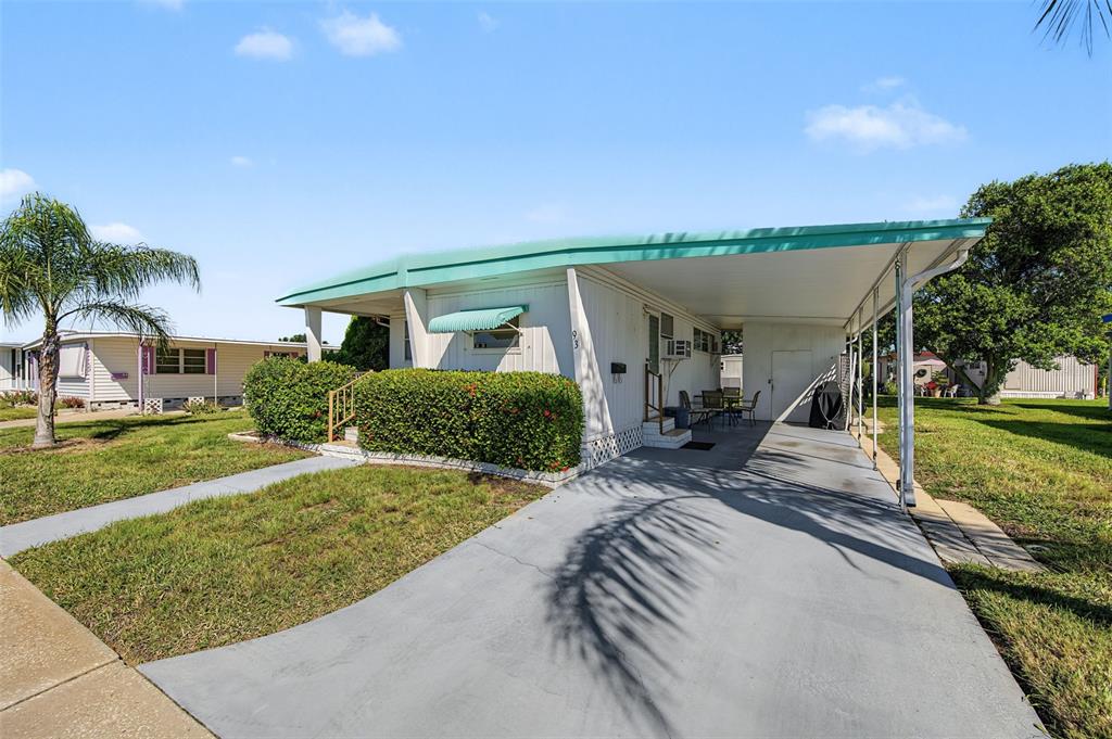 A covered patio features two floral-patterned chairs, a small side table, and a white door — 93 RACHEL DRIVE, TARPON SPRINGS, FL