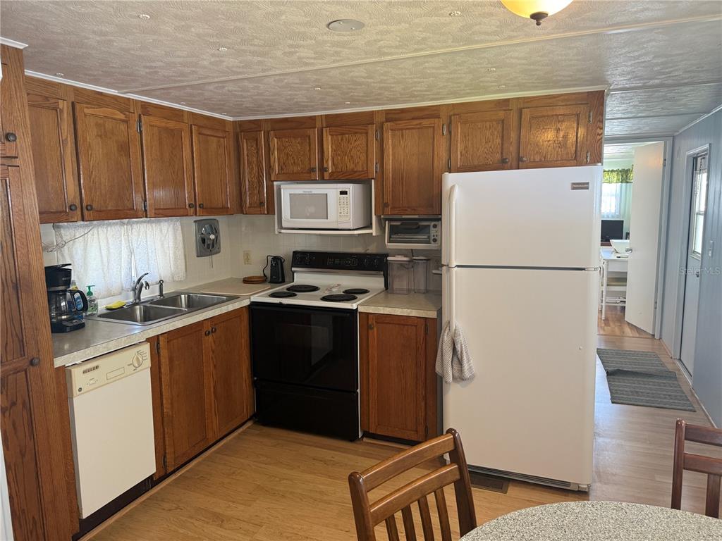 A kitchen features wood cabinets, white appliances, a double sink, and light-colored laminate flooring — 731 CAMELLIA DRIVE, VENICE, FL