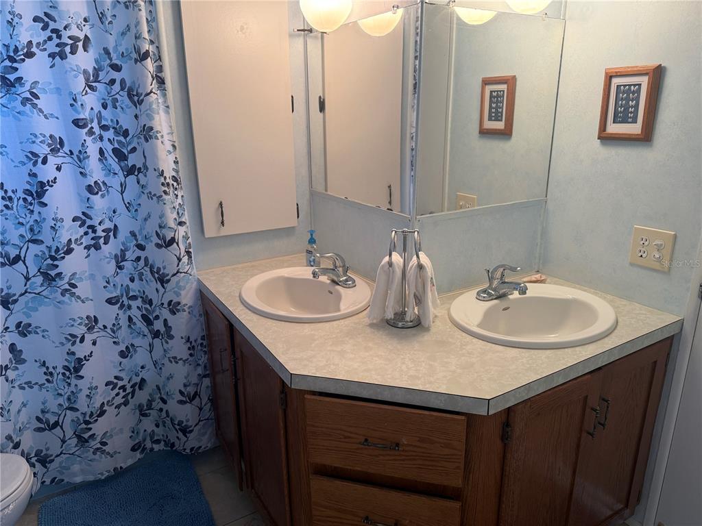 A bathroom features a double-sink vanity with wood cabinets, a laminate countertop, and a shower curtain — 731 CAMELLIA DRIVE, VENICE, FL