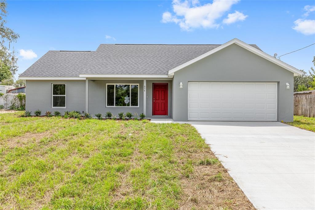 A single-story gray house features a red front door and a two-car garage — 654 NE 130TH COURT, SILVER SPRINGS, FL