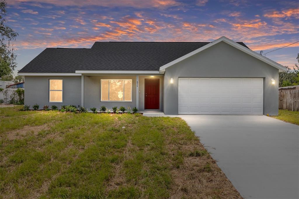 A single-story gray house with a red front door, white garage door, and dark roof — 654 NE 130TH COURT, SILVER SPRINGS, FL