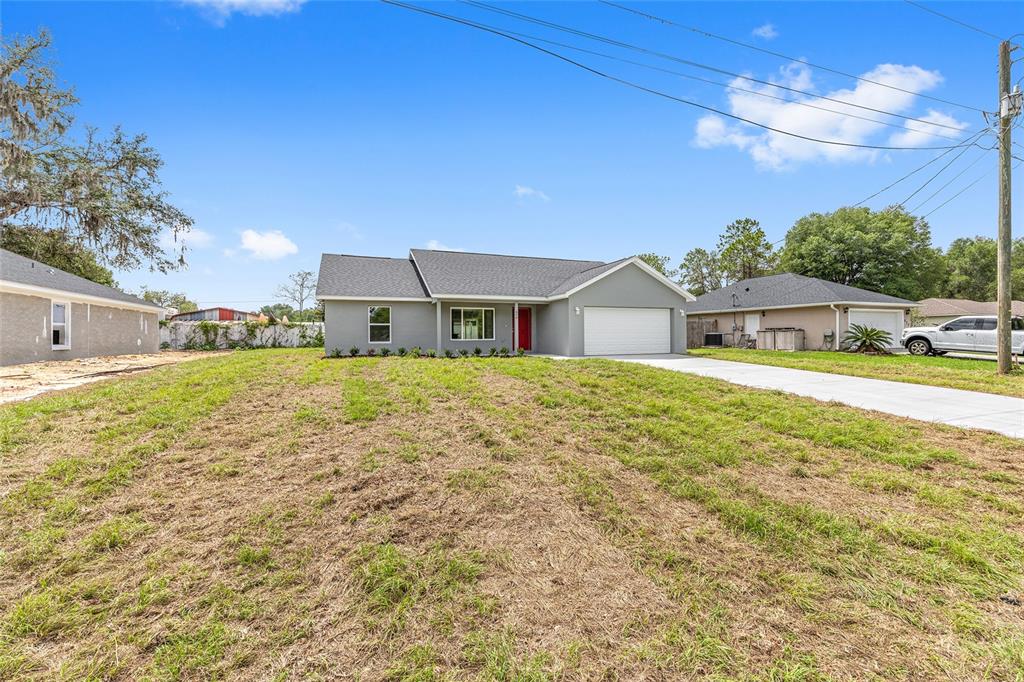 A gray single-story house with a white garage door and a large grassy front yard — 654 NE 130TH COURT, SILVER SPRINGS, FL