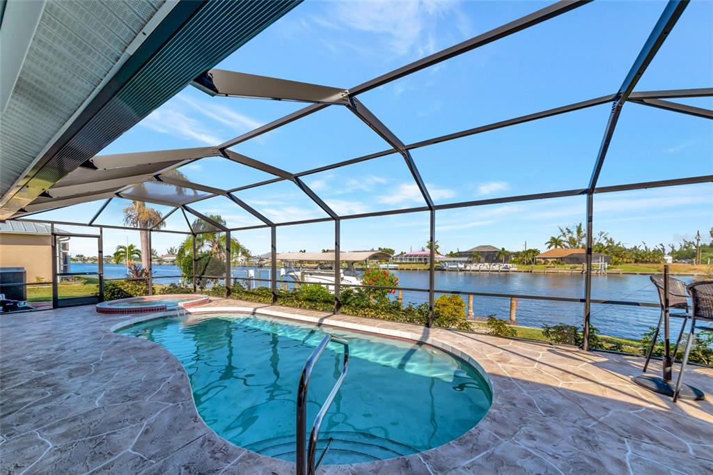 A screened-in pool and spa overlook a canal with a boat dock and surrounding homes — 15564 RUSTON CIRCLE, PORT CHARLOTTE, FL