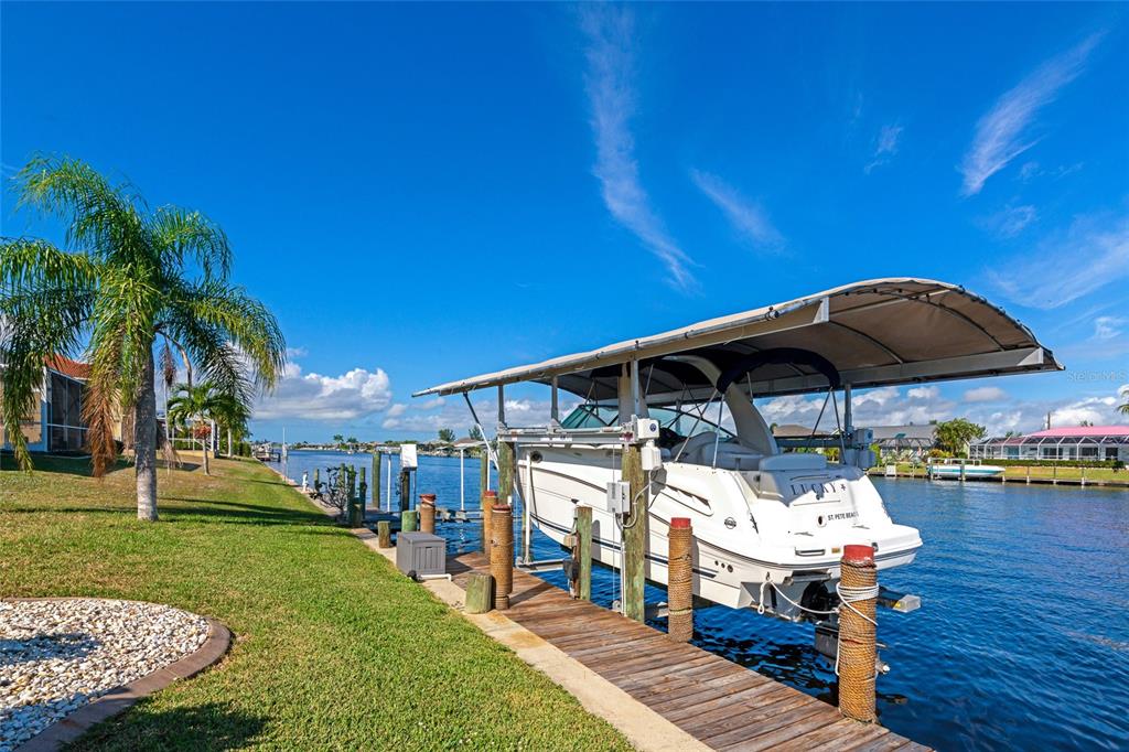 A boat on a lift is docked at a grassy waterfront property under a blue sky — 15564 RUSTON CIRCLE, PORT CHARLOTTE, FL