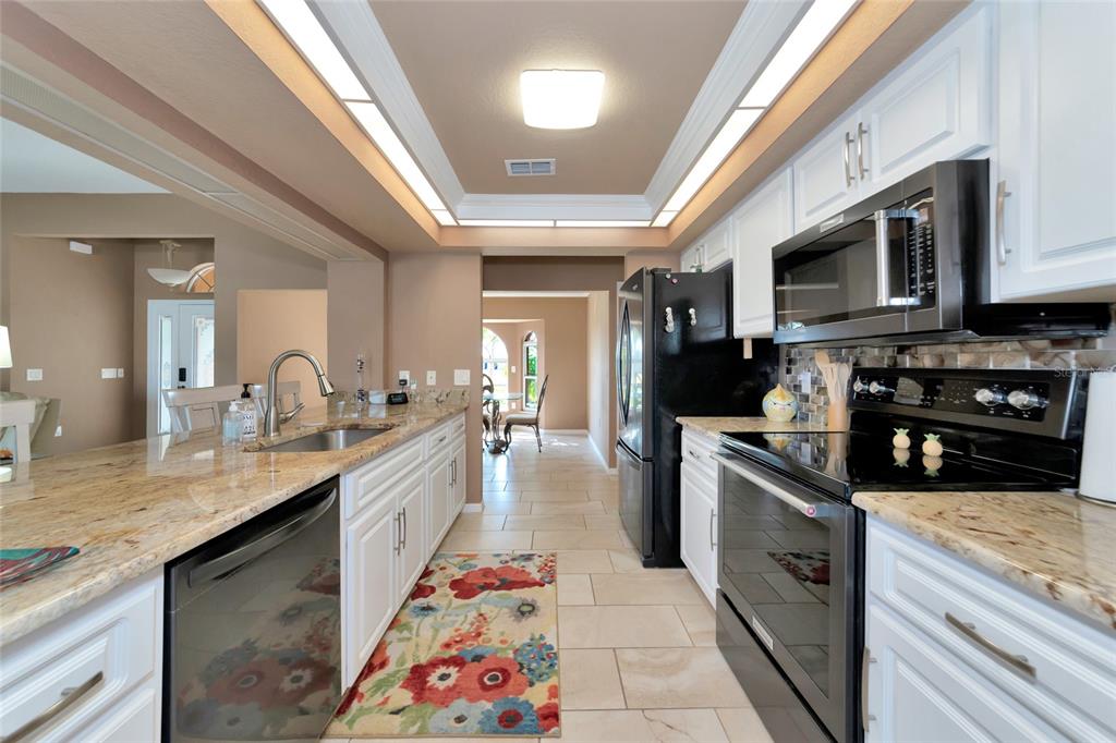 A kitchen features white cabinets, granite countertops, black appliances, and a floral runner rug — 15564 RUSTON CIRCLE, PORT CHARLOTTE, FL