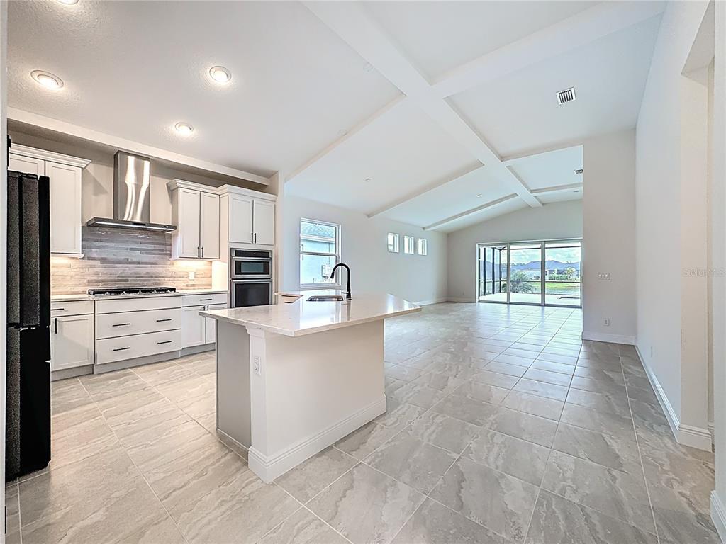 A modern kitchen with white cabinets and a center island opens into a spacious living area — 4214 SEA MARSH PLACE, PARRISH, FL