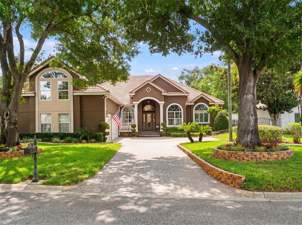 A two-story brown stucco house with a paved driveway and mature trees in the front yard — 9223 HIDDEN BAY LANE, ORLANDO, FL