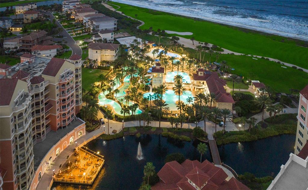 An aerial view shows a resort complex with swimming pools, palm trees, and a pond — 200 OCEAN CREST DRIVE UNIT 137, PALM COAST, FL