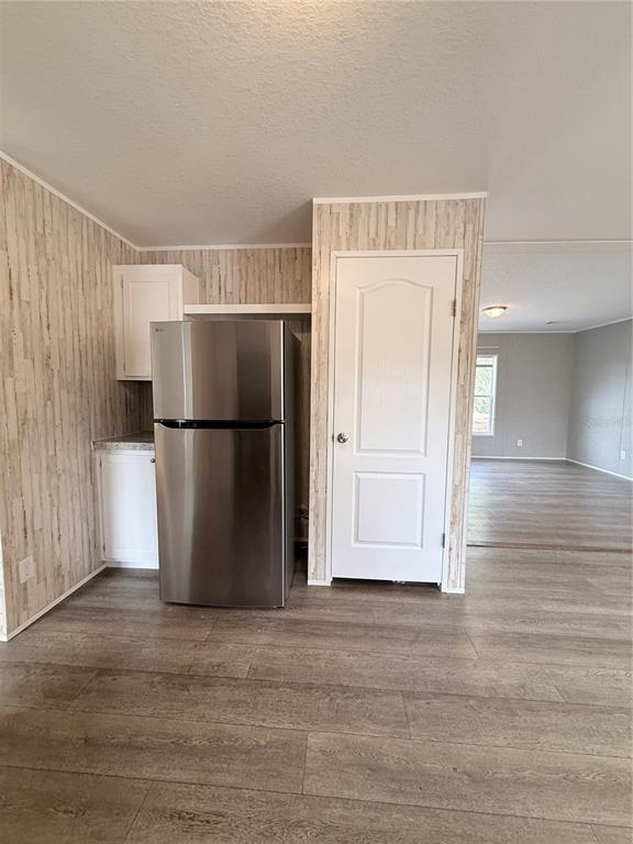 A kitchen area features a stainless steel refrigerator, white cabinets, and light wood-look flooring — 932 SE 40TH PLACE, MELROSE, FL