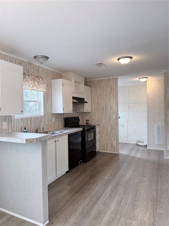 A kitchen features white cabinets, black appliances, wood-look flooring, and vertical wood-paneled walls — 932 SE 40TH PLACE, MELROSE, FL