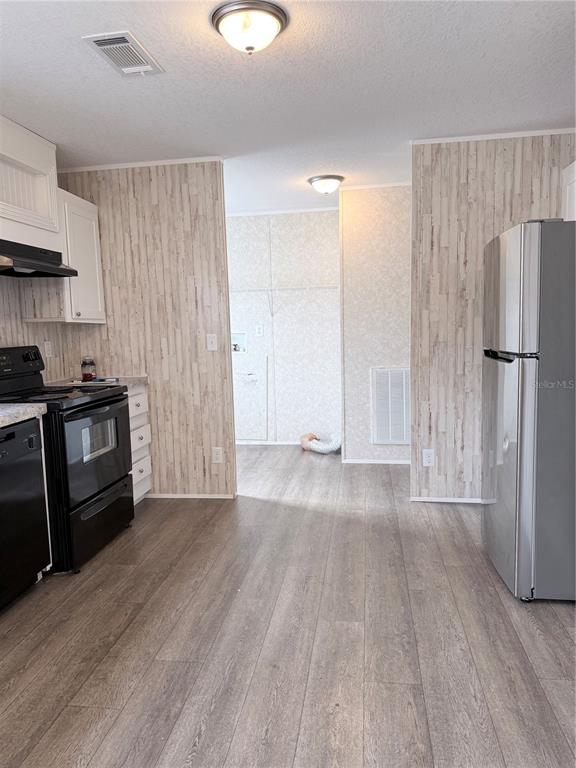 A kitchen features wood-look flooring, light-colored paneling, black appliances, and a stainless steel refrigerator — 932 SE 40TH PLACE, MELROSE, FL