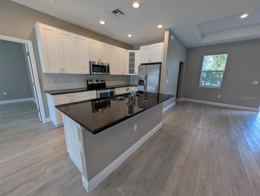 A kitchen features white cabinets, black countertops, a center island, and light wood-look flooring — 1643 JEANNIN DRIVE, NORTH PORT, FL