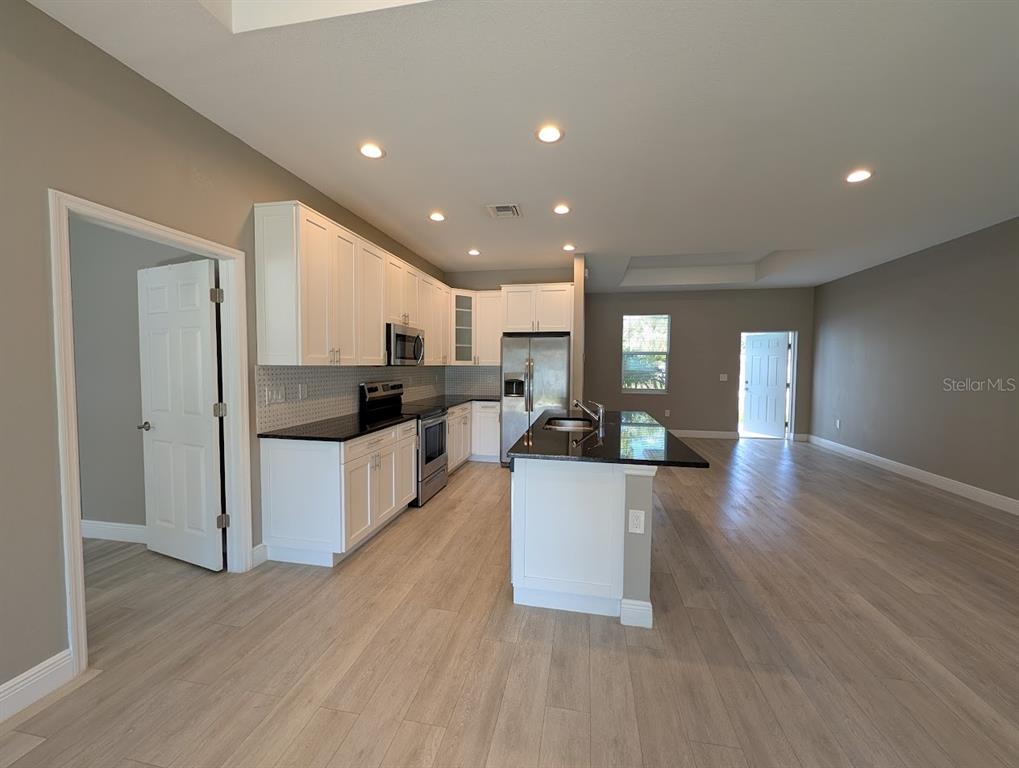 A kitchen with white cabinets, black countertops, and light wood-look flooring opens to a living area — 1643 JEANNIN DRIVE, NORTH PORT, FL