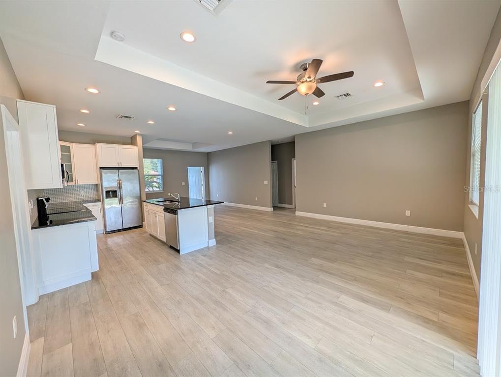 An open-concept kitchen and living area feature white cabinets, black countertops, and light wood flooring — 1643 JEANNIN DRIVE, NORTH PORT, FL
