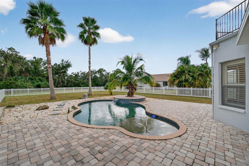 A backyard features a kidney-shaped pool with a waterfall, palm trees, and a brick patio — 3870 155TH AVENUE E, PARRISH, FL