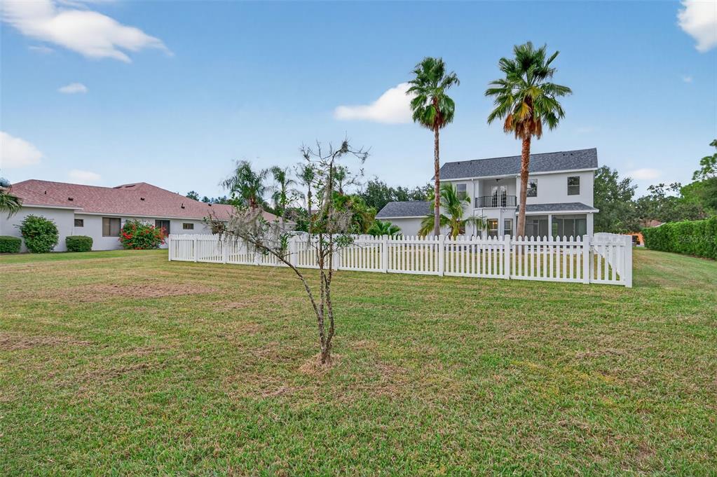 A white picket fence encloses a backyard with a small tree and two palm trees — 3870 155TH AVENUE E, PARRISH, FL