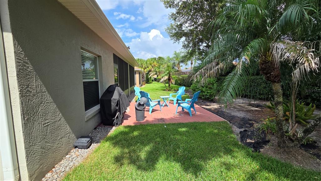 A patio with blue chairs and a grill sits beside a house with a lawn — 4063 BIRKDALE DRIVE, LAKE WALES, FL