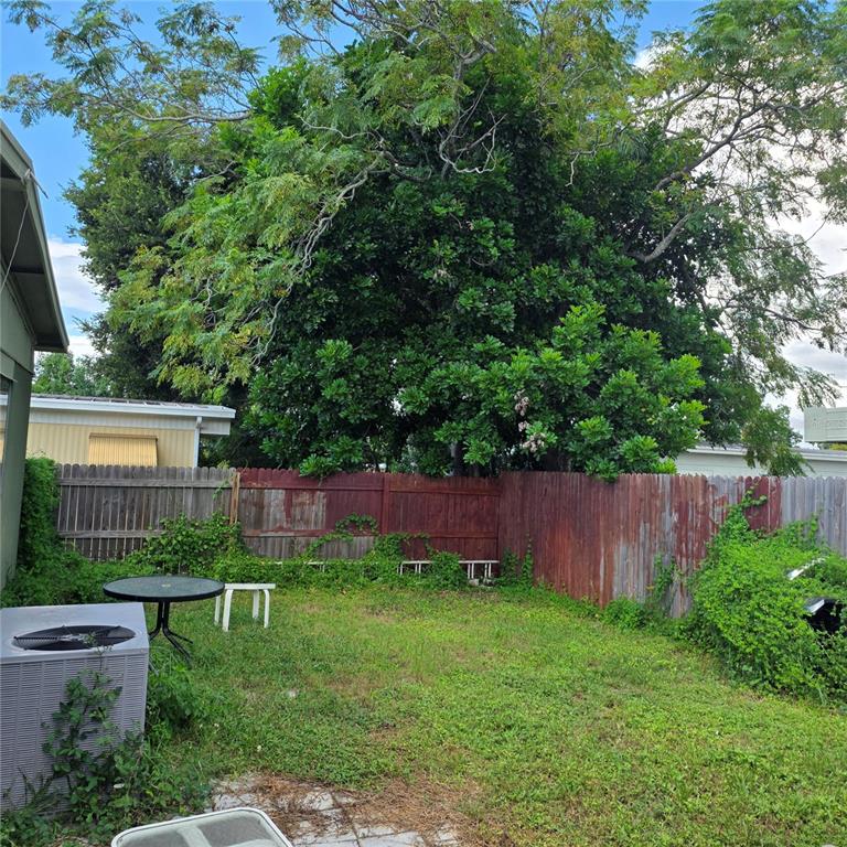 A backyard features a small patio, a round table, a wooden fence, and a large tree — 4122 CARDOON DRIVE, NEW PORT RICHEY, FL