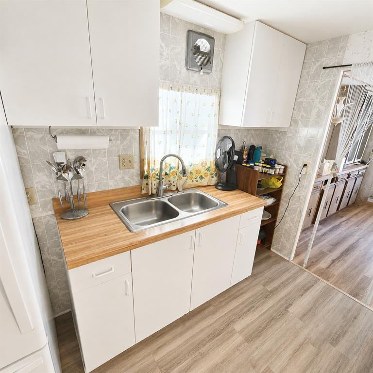 A kitchen features white cabinets, a wood-look countertop, a double sink, and tiled walls — 4122 CARDOON DRIVE, NEW PORT RICHEY, FL