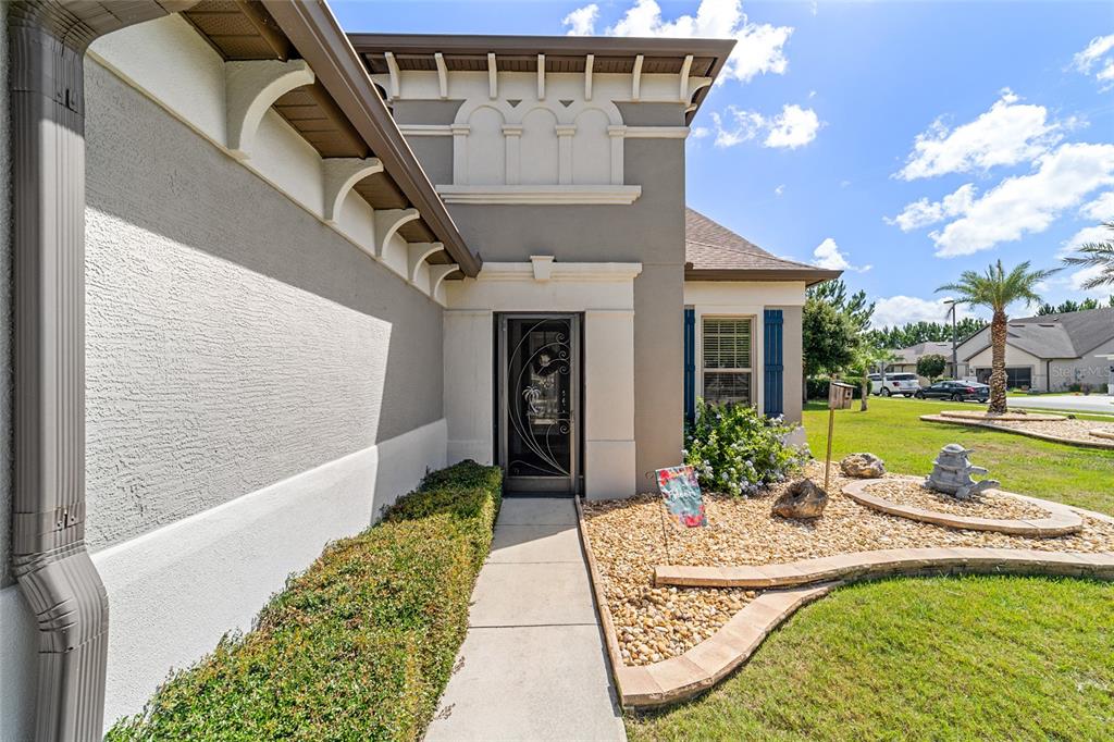 A front entryway with a glass storm door, stucco walls, and a landscaped rock garden — 9300 SW 70TH LOOP, OCALA, FL