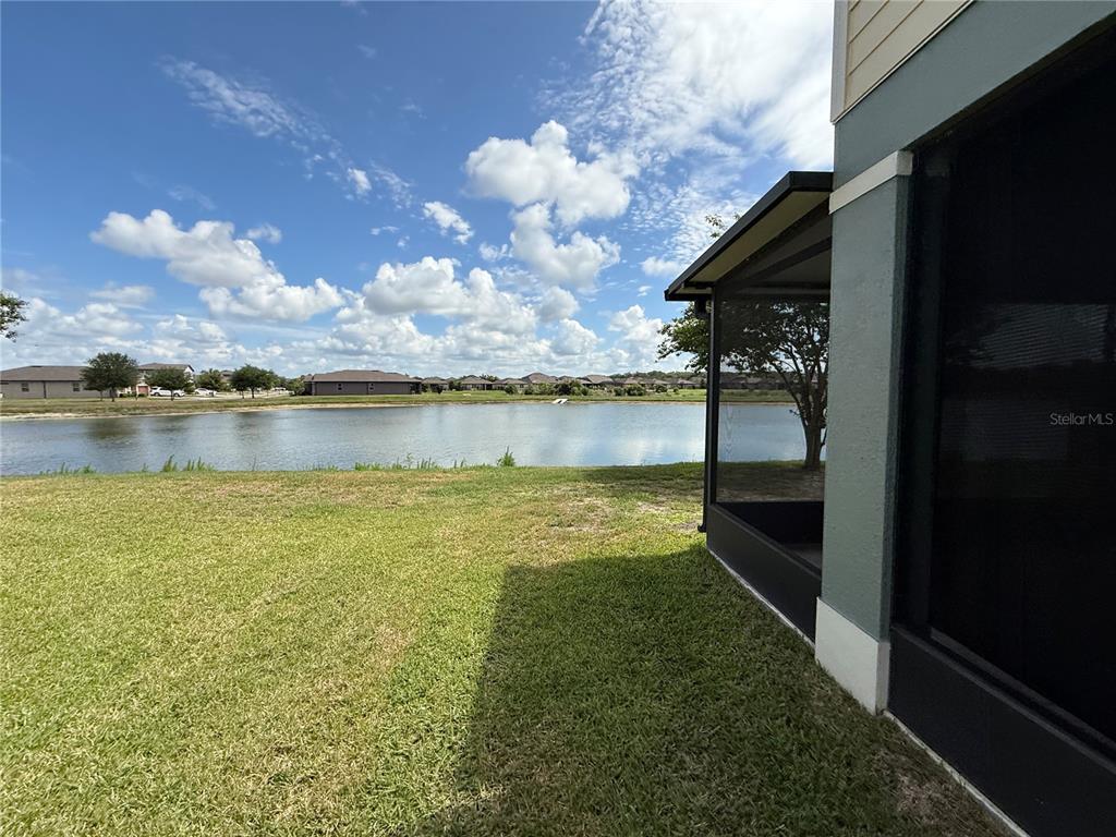 A view of a grassy backyard overlooking a lake with a screened-in patio area — 9154 HILLCROFT DRIVE, RIVERVIEW, FL