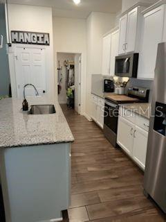 A kitchen with white cabinets, granite countertops, a kitchen island, and wood-look flooring — 8083 GUILD WAY, JACKSONVILLE, FL