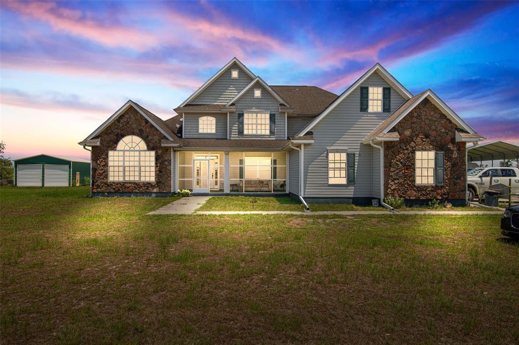 A two-story house with stone accents, gray siding, and a screened-in front porch at dusk — 732 SE SIDE WHEEL TRAIL, LEE, FL