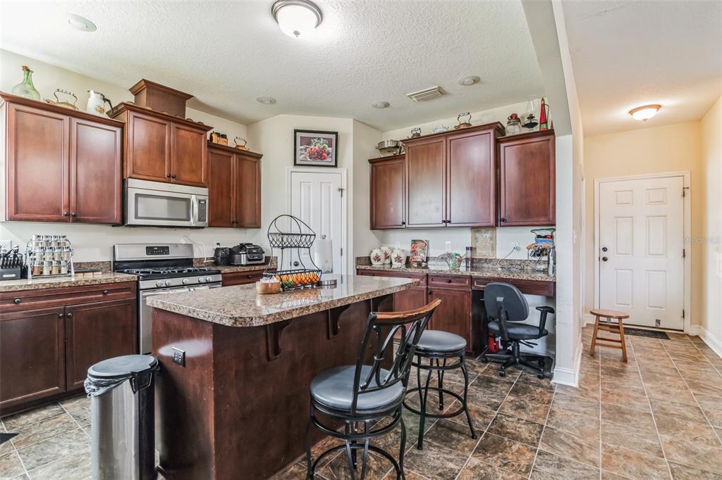 A kitchen features dark wood cabinets, granite countertops, a central island, and tiled flooring — 732 SE SIDE WHEEL TRAIL, LEE, FL