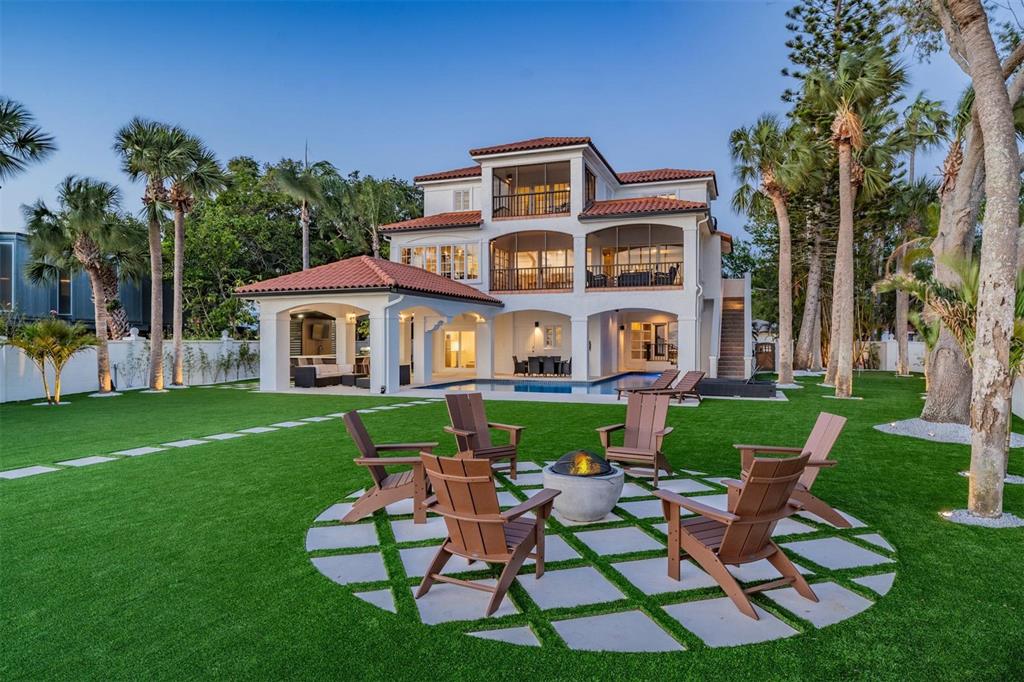 A three-story house with a pool, patio, and fire pit area in a grassy backyard — 128 CARLYLE DRIVE, PALM HARBOR, FL