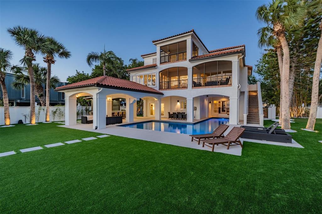 A three-story house with a tiled roof, screened balconies, a swimming pool, and a lawn — 128 CARLYLE DRIVE, PALM HARBOR, FL