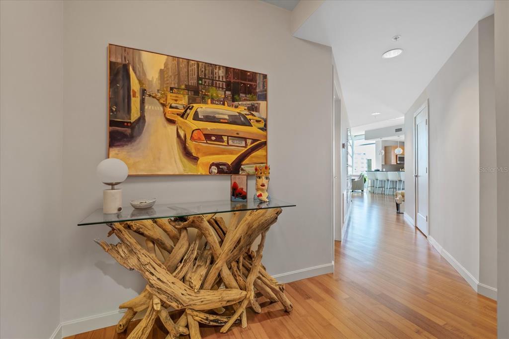 A hallway features a glass-topped driftwood console table, a city street painting, and hardwood floors — 400 4TH AVENUE S UNIT 1004, ST PETERSBURG, FL