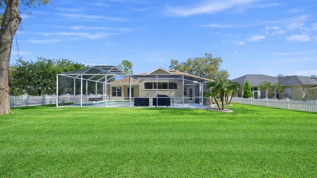 A backyard features a large green lawn, a white fence, and a screened-in pool area — 3209 PARTRIDGE POINT TRAIL, VALRICO, FL