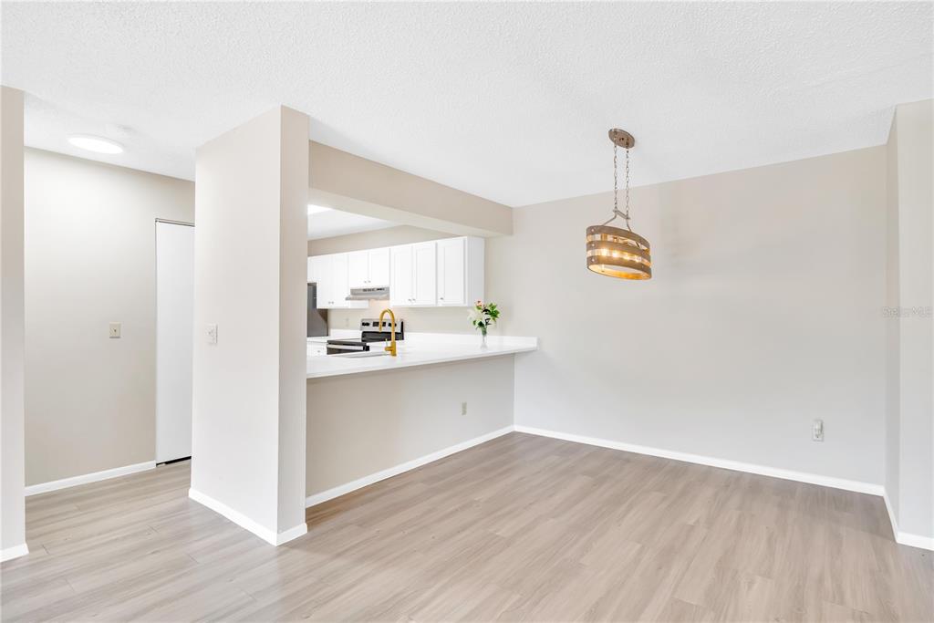 A dining area with wood-look flooring opens to a kitchen featuring white cabinets and counters — 612 KENWICK CIRCLE UNIT 103, CASSELBERRY, FL