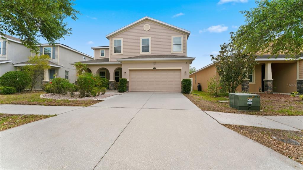 A two-story suburban house with beige siding, a two-car garage, and a concrete driveway — 11620 WARREN OAKS PL, RIVERVIEW, FL