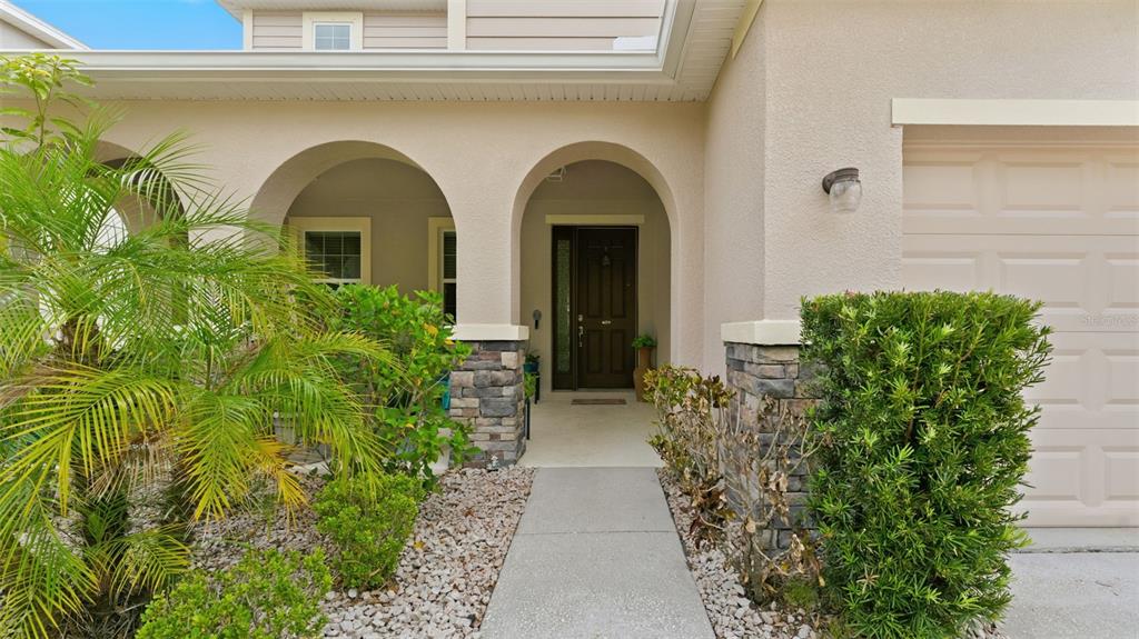 A concrete walkway leads to the arched entryway of a house with stone accents — 11620 WARREN OAKS PL, RIVERVIEW, FL