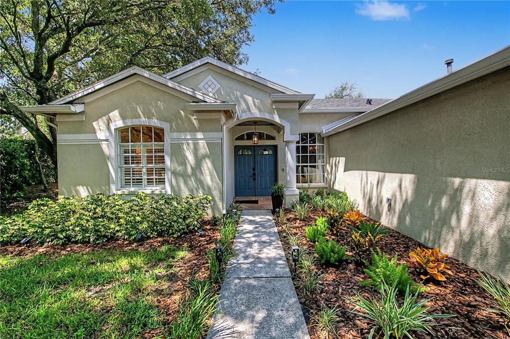 The exterior of a single-story home features a blue double door and a concrete walkway — 9402 HUNTERS POND DRIVE, TAMPA, FL