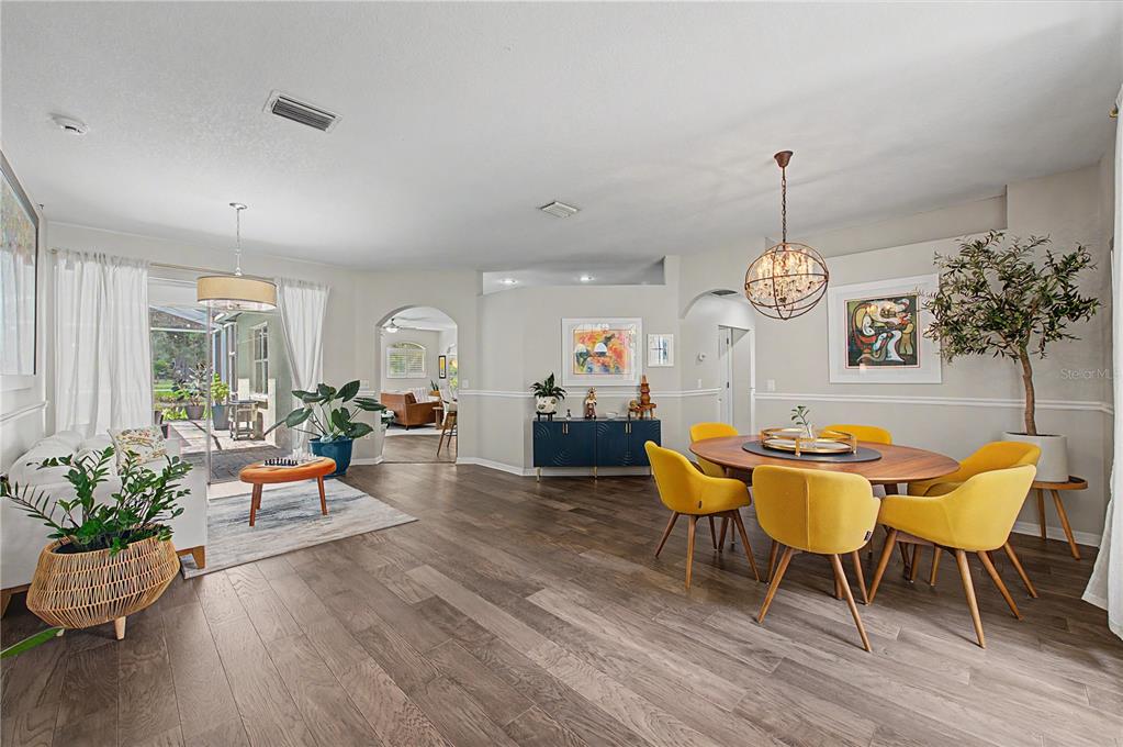 An open-concept dining and living area features wood-look flooring, yellow chairs, and a crystal chandelier — 9402 HUNTERS POND DRIVE, TAMPA, FL