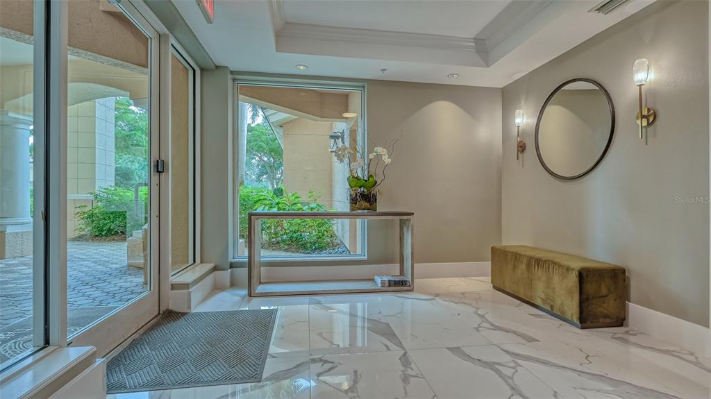 A bright entryway features white marble floors, a console table, a bench, and glass doors — 401 N POINT ROAD UNIT 301, OSPREY, FL