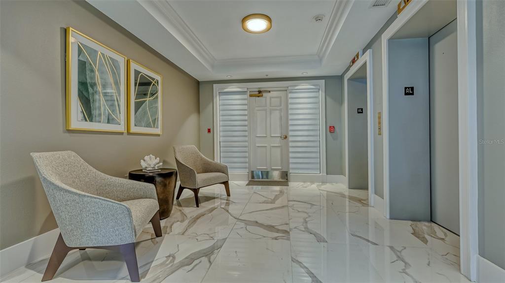 A modern lobby features marble floors, two armchairs, framed wall art, and two elevator doors — 401 N POINT ROAD UNIT 301, OSPREY, FL