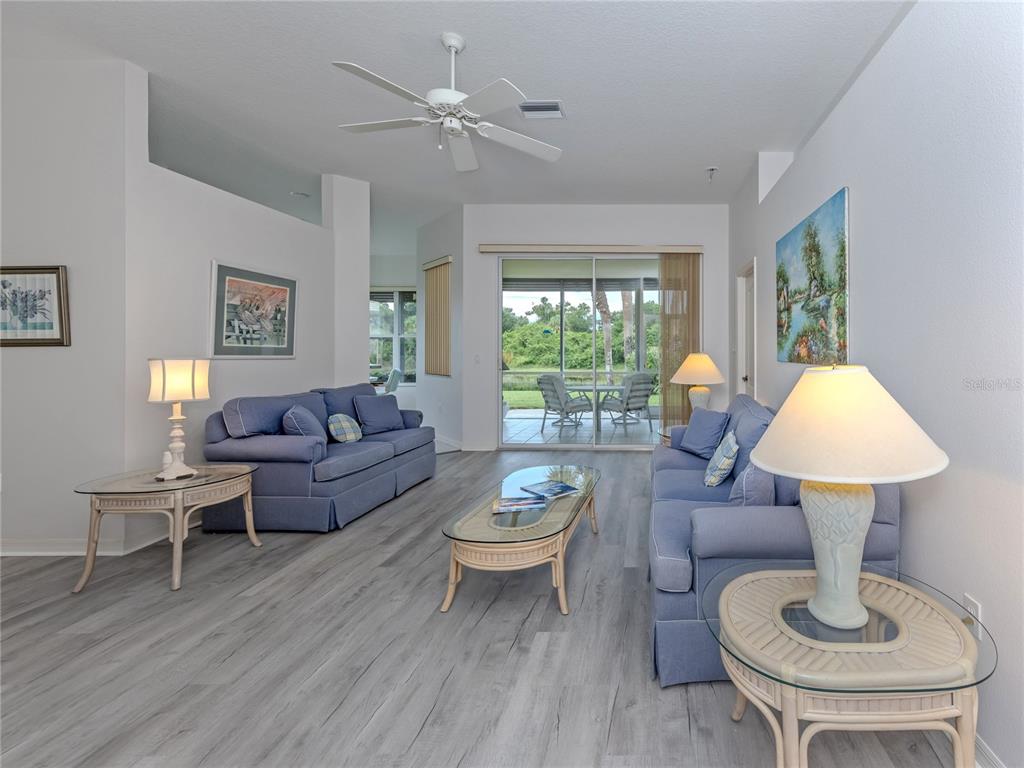 A living room features blue sofas, glass-topped rattan tables, a ceiling fan, and sliding glass doors — 737 POND LILY WAY, VENICE, FL