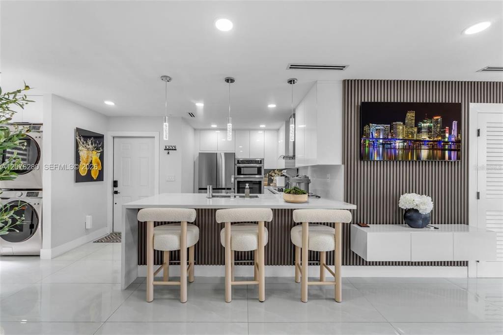 A modern kitchen features a white island with three stools and a slatted accent wall — 1180 NW 124TH PLACE UNIT 208, MIAMI, FL