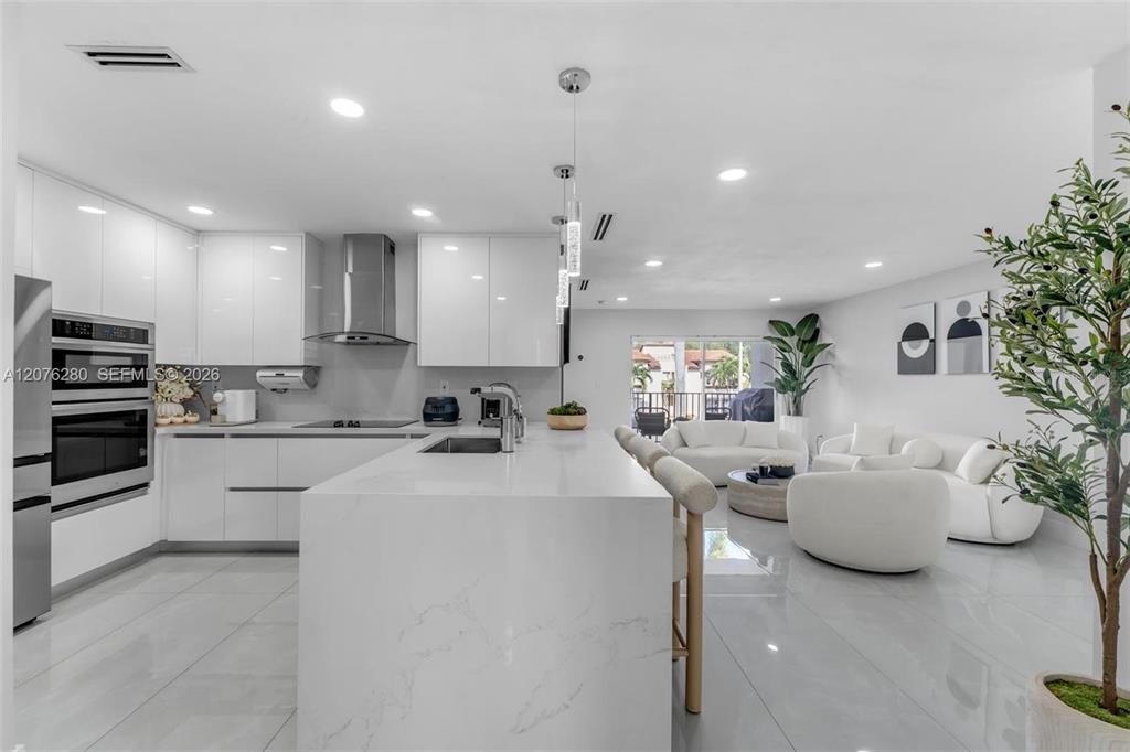 A modern open-concept kitchen and living area features white cabinetry, marble countertops, and tiled floors — 1180 NW 124TH PLACE UNIT 208, MIAMI, FL